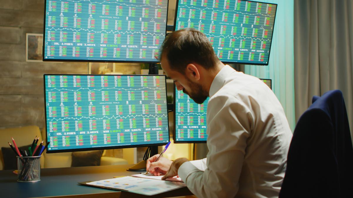 bearded-businessman-taking-notes-while-checking-stock-market-from-home-office.jpg
